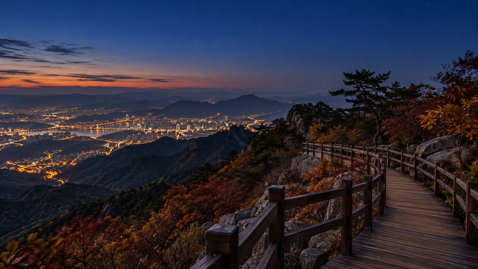 해 진 뒤 산 능선의 나무 데크 탐방로 너머로 불빛이 반짝이는 도시 야경